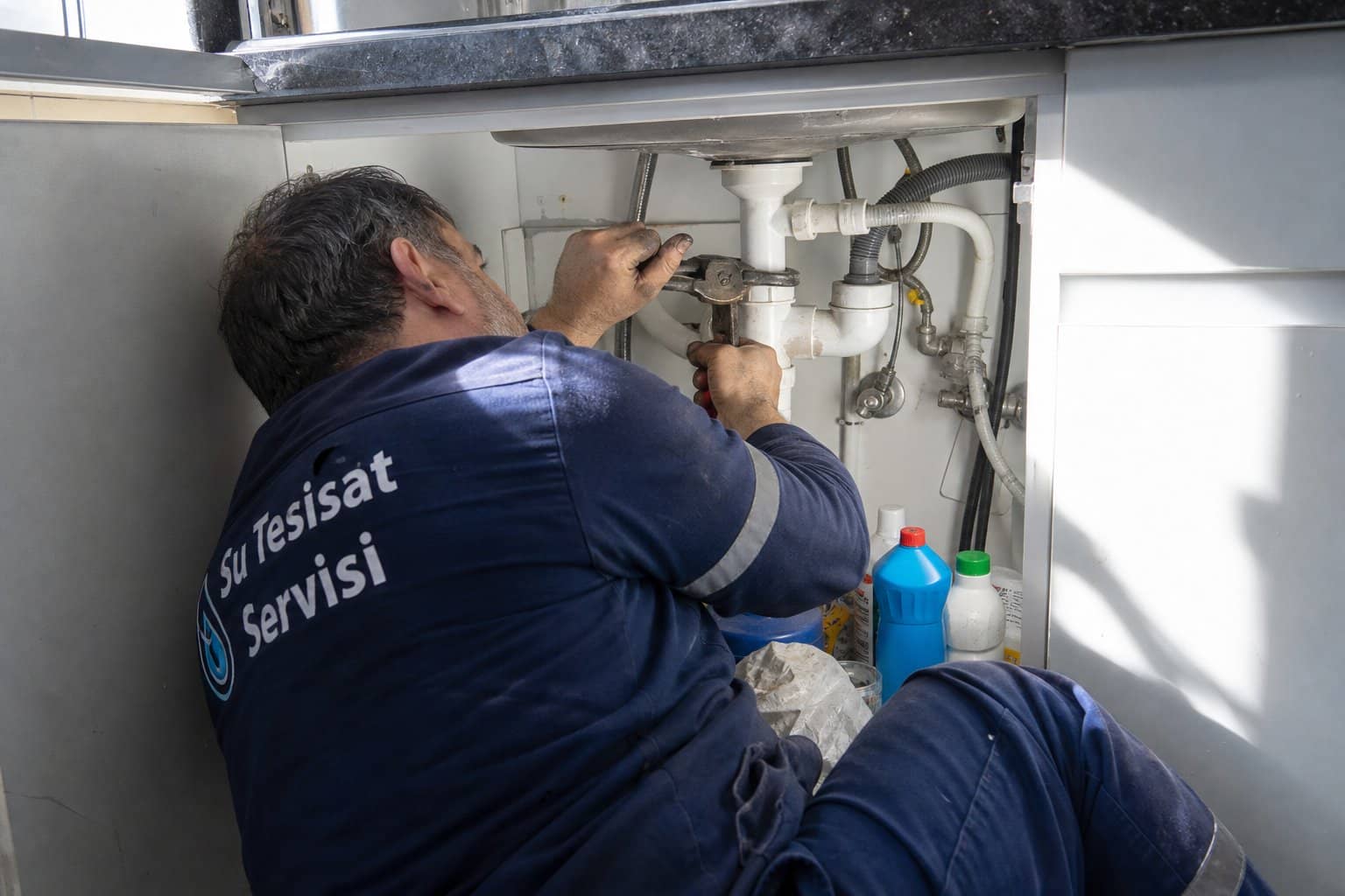 lavabo altinda boru anahtariyla boru tamir eden tesisatci